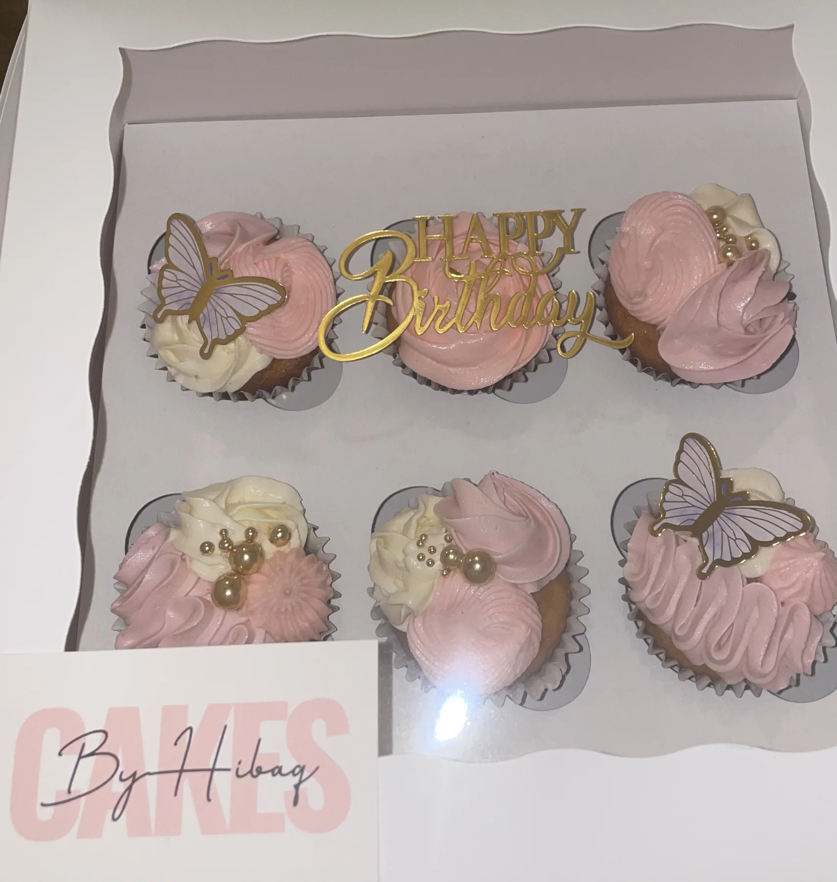 Pink and white cupcakes presented in a box with a Cakes by Hibaq card