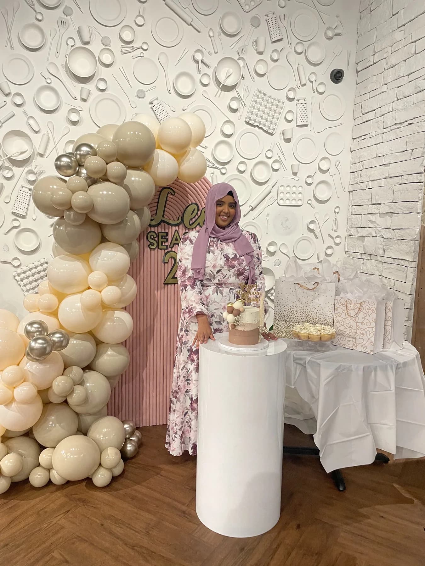 Hibaq standing beside her cake display and balloon installation