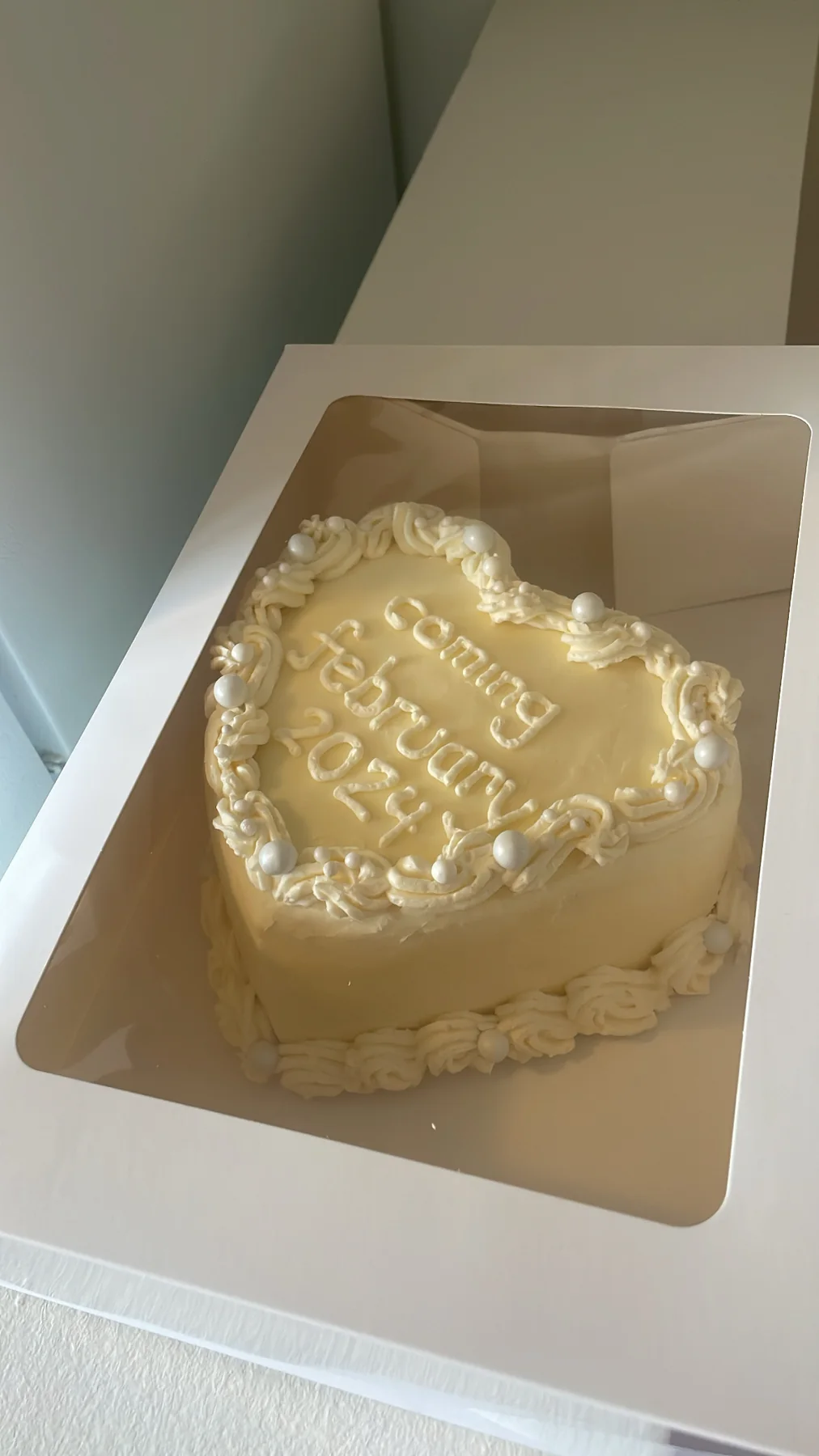 White heart-shaped cake with delicate vintage piping inside a cake box